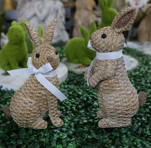Detail of two rabbit statues with woven texture and white ribbon bows for garden decor