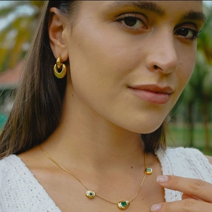 Detail of model wearing golden hoop earrings and a gemstone necklace set against nature