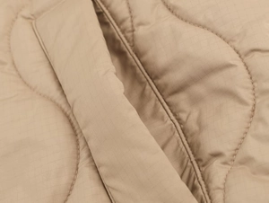 Detail of light khaki quilted fabric showing ripstop pattern and wave stitching on the jacket