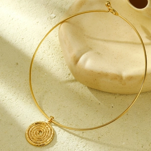 Macro shot of a golden rigid choker necklace with a spiral textured round pendant