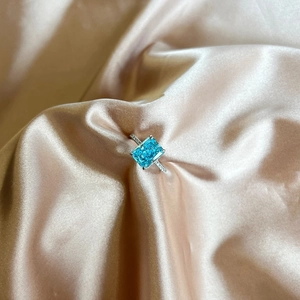Close-up of S925 silver ring with blue-green square zircon on pink silk fabric