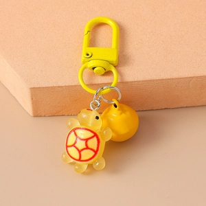 Detail of yellow turtle keychain featuring resin turtle charm and metal bell accessory