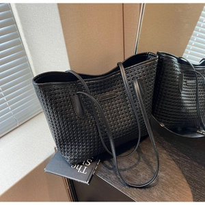 Detail of black woven leather tote bag shown on a sleek surface with soft lighting