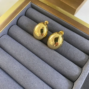 Detailed view of polished gold oval stud earrings resting in a gray velvet jewelry box