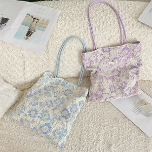 Close-up of floral embroidery on blue and purple canvas tote bags on a soft rug