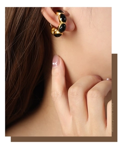Detail view of gold-plated titanium earrings with black oval glaze inserts on a model