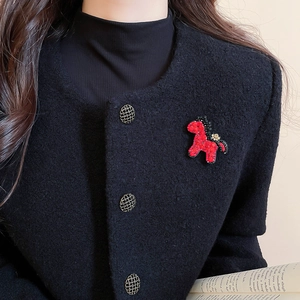 Detailansicht einer roten Perlenbrosche in Pferdeform auf einer schwarzen Tweedjacke
