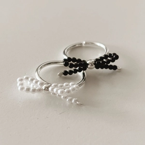 Detail of 925 silver bow rings featuring black beads and white pearls on ivory surface