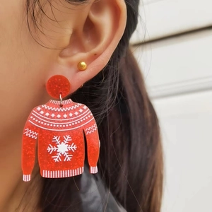 Festive red acrylic Christmas sweater earrings with glitter snowflakes worn by model