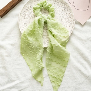 Detail of light green hair scrunchie with long ribbons on embossed white plate