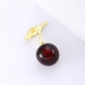 Détail de l'élégante broche cerise avec perles rouges et tige dorée texturée