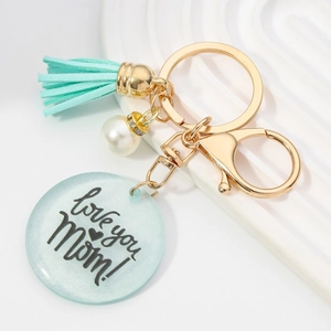 Détail d'un porte-clés doré avec pompon bleu sarcelle, perle et disque gravé