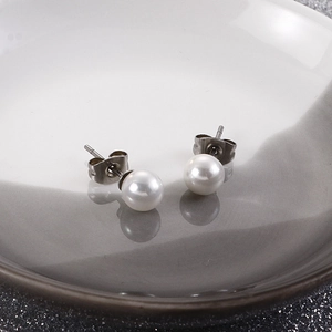Detailed view of white round pearl earrings on a ceramic dish with glitter background