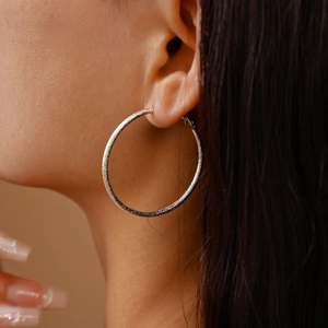 Close-up of silver hoop earrings with a frosted textured finish worn by a model