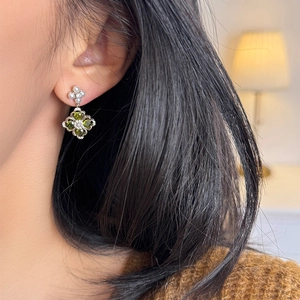 Close-up of four-leaf clover drop earrings with green stones and pearls on model