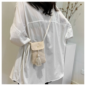 Detail of a beige woven crossbody bag with flip cover and stylish tassel detail
