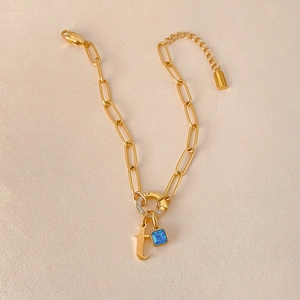 Detail van een 14K vergulde paperclip armband met blauwe edelsteen en initiaal f hanger