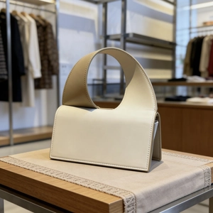Minimalist beige leather crossbody bag with wide shoulder strap on wooden display