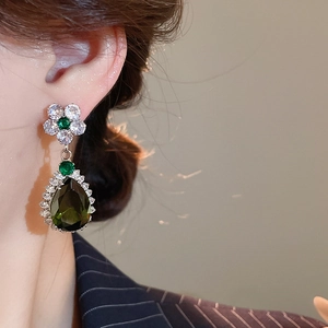 Dettaglio macro di eleganti orecchini a fiore con zircone verde a goccia su modella