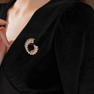 Detailed view of a gold C-shaped brooch featuring lustrous pearls and zircon on black velvet