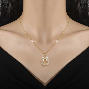 Detail of gold necklace featuring white enamel bow and baguette-cut crystal pendant on model