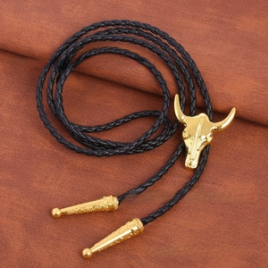 Detail of a gold bull skull bolo tie with black braided leather and ornate metal tips
