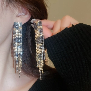 Close-up of sparkling leopard print rhinestone tassel earrings on model in gold and grey