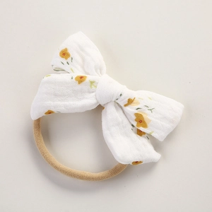 Détail du bandeau bébé en mousseline blanche avec nœud à fleurs jaunes et ruban élastique