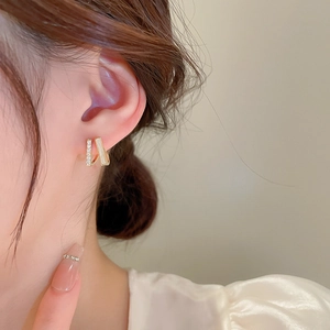Model wearing gold parallel bar rhinestone earrings against a warm beige background