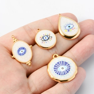Golden white enamel evil eye pendants in various geometric shapes held by hand