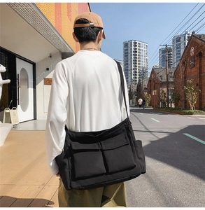 Outdoor shot of a black canvas messenger bag with large front utility pockets