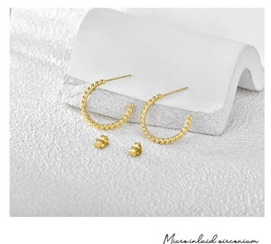 Detailed close-up of 18K gold plated twisted hoop earrings on white stone display