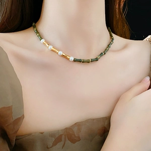 Dettaglio di una collana vintage con giada verde a forma di bambù e perle bianche