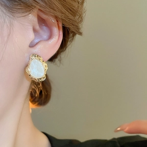 Macro detail of vintage gold hammered earring with white marble texture on a model