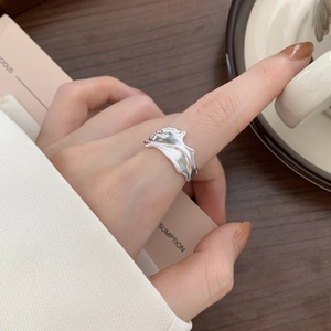 Close-up of wavy fluid silver ring on finger with coffee and magazine lifestyle setting
