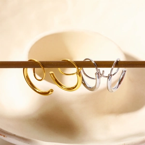 Artistic detail of minimalist gold and silver spiral hoop earrings on a wooden display