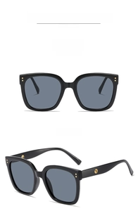 Detail of black square sunglasses featuring dark grey lenses and golden dot rivets