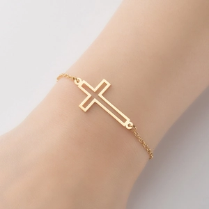 Detailed close-up of a hollow-out cross pendant on a minimalist gold stainless steel bracelet