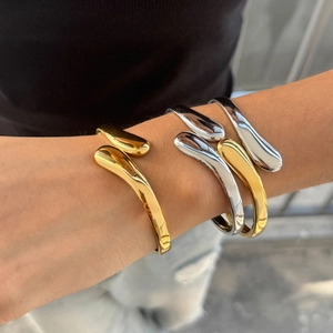 Polished gold and silver fluid open cuff bracelets shown on wrist in a stacked style