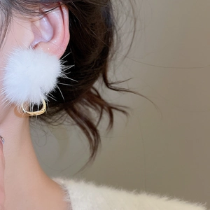 Detail of elegant white fur ball earrings with golden rings worn on a female model