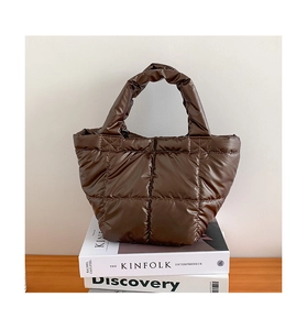 Detail of dark brown quilted puffer tote bag with ruched handles on a soft minimalist background