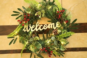 Close-up of lighted Christmas wreath with pine needles, berries, and wooden welcome sign