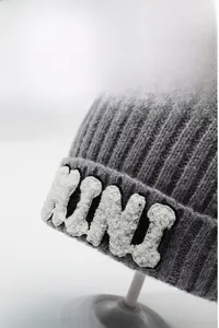 Detail of dark grey knit beanie with white plush KINI embroidery on the cuff