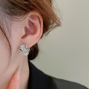 Macro view of silver geometric earrings with irregular liquid ripple texture on ear