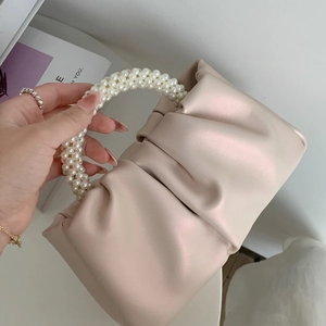 Detail of cream pleated cloud bag featuring a glossy faux pearl handle and leather texture