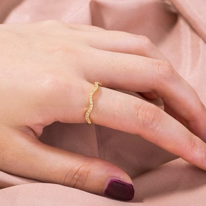 Detail shot of a wavy 18K gold ring with zircons worn on index finger over silk fabric