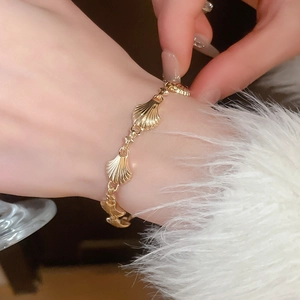 Detail shot of a vintage gold shell bracelet with polished finish worn on a woman's wrist