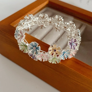 Detail of colorful enamel flower charms on an elastic bracelet on a wooden tray