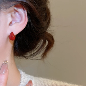 Detailed close-up of glossy red teardrop earrings on model with a warm aesthetic
