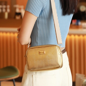Golden chevron crossbody camera bag with wide strap worn by model in a cafe setting